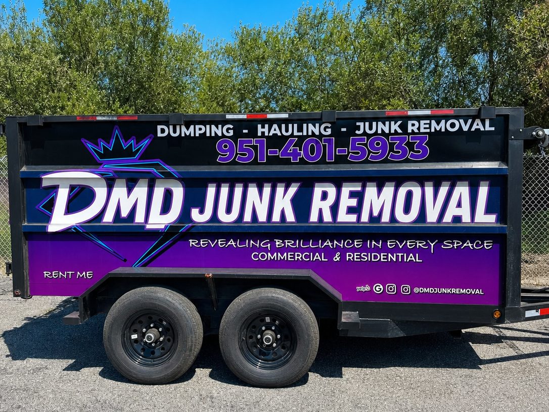 La segunda traila de DMD, una traila de dompe morada más vieja de DMD Junk Removal, estacionada de lado frente a una fila de árboles