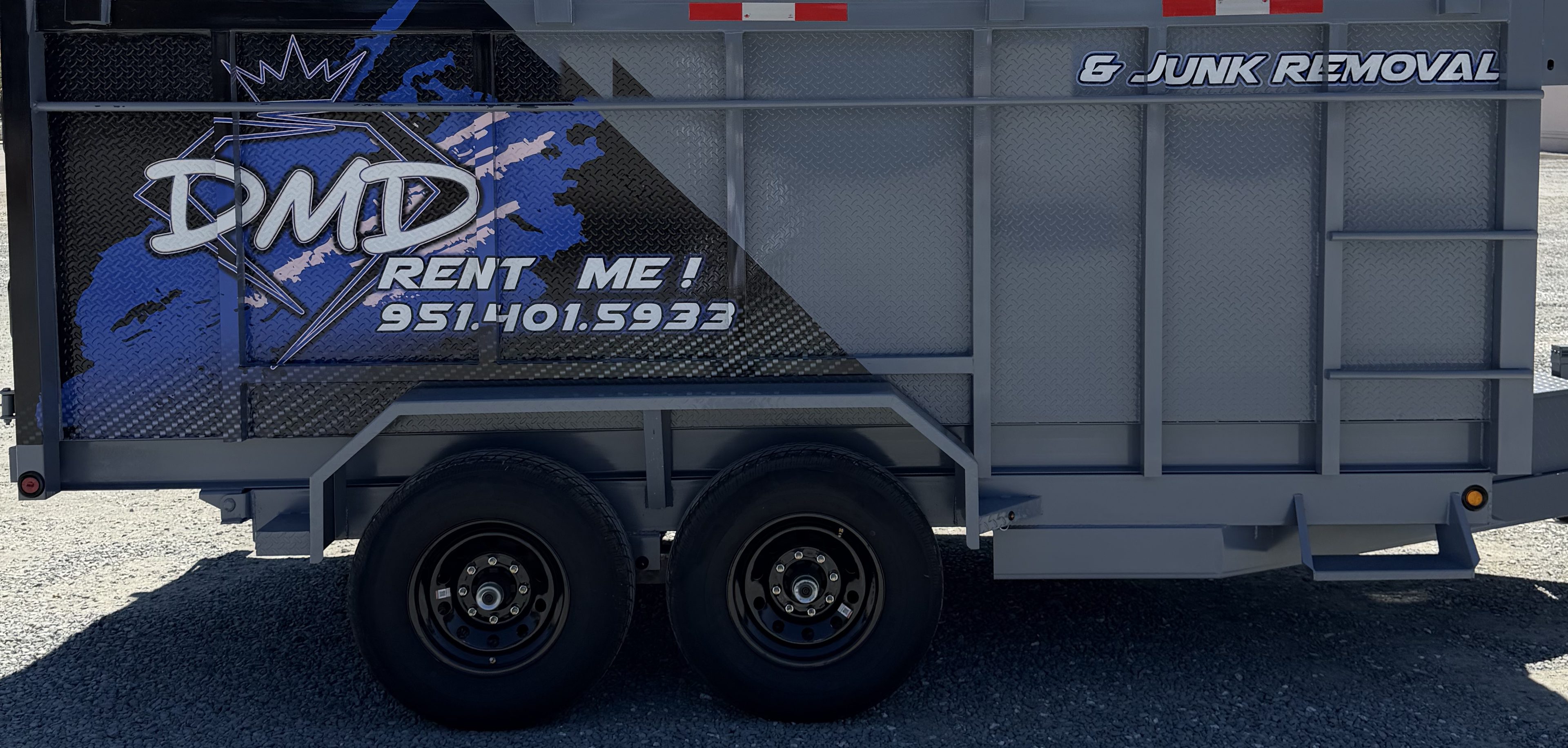 DMD 14 ft dump trailer side-on with the blue DMD wrap, the DMD logo panel and both axles