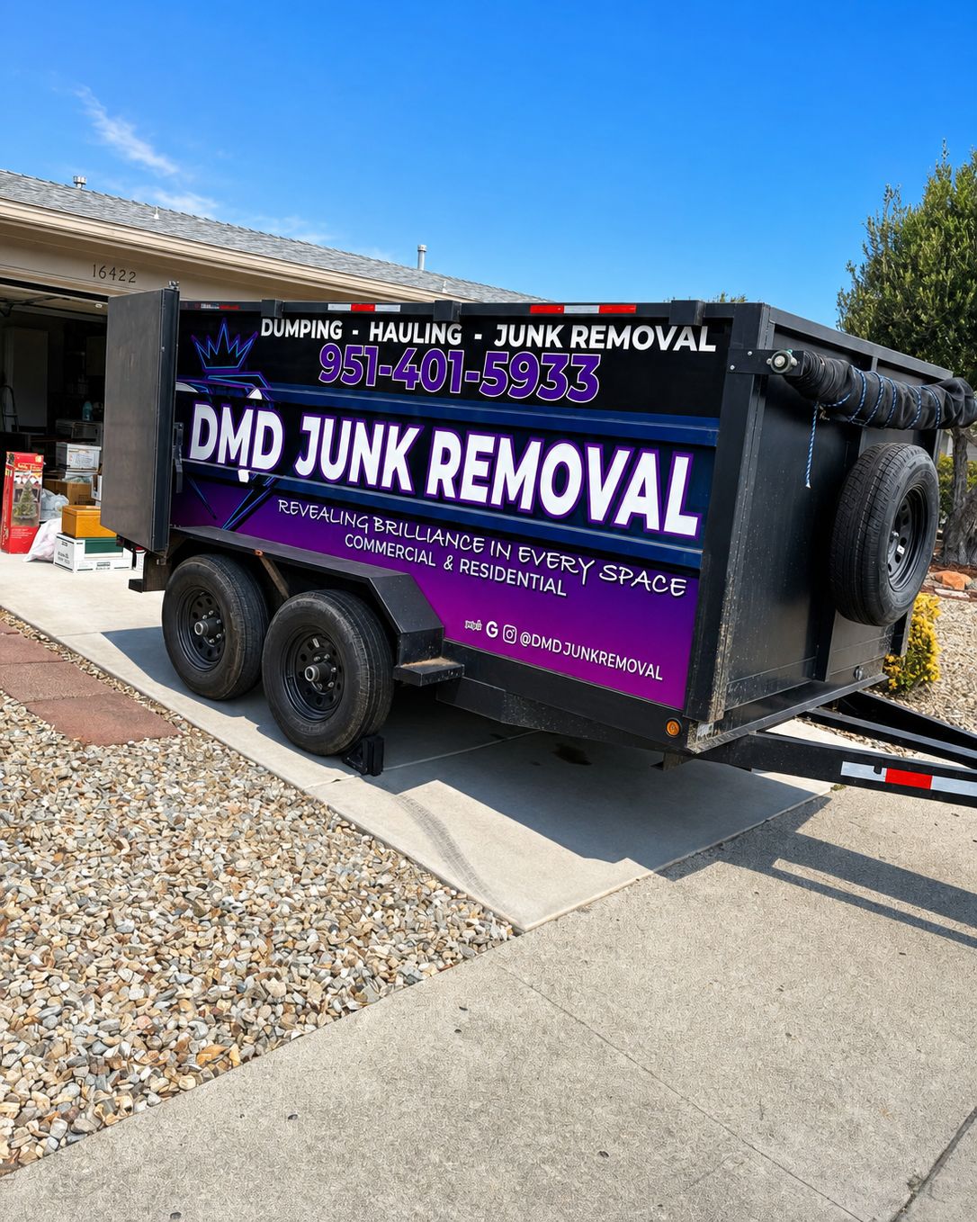 DMD dump trailer parked on a residential driveway, DMD JUNK REMOVAL wrap and phone number 951-401-5933 facing the street