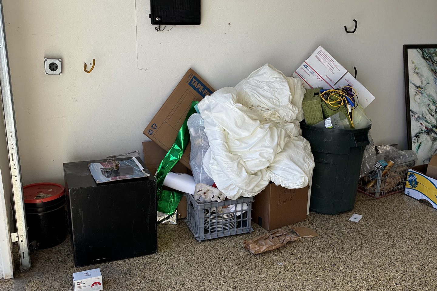 A residential garage cleanout in progress — boxes, bedding, bins and a mini fridge staged for haul-off