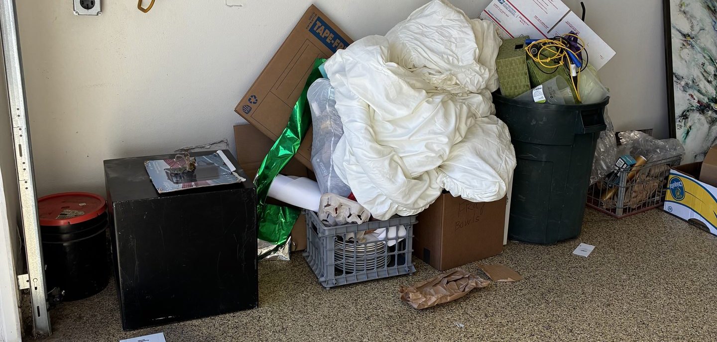 A residential garage cleanout in progress — boxes, bedding, bins and a mini fridge staged for haul-off