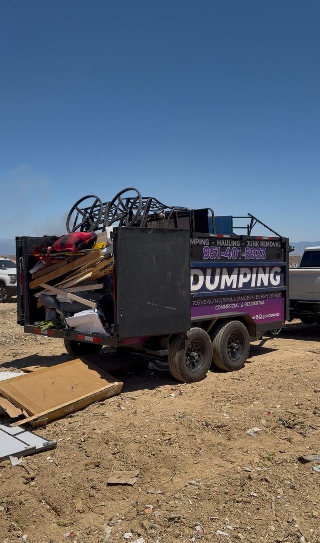 A DMD dump trailer loaded with lumber and wrought-iron patio furniture parked at the landfill