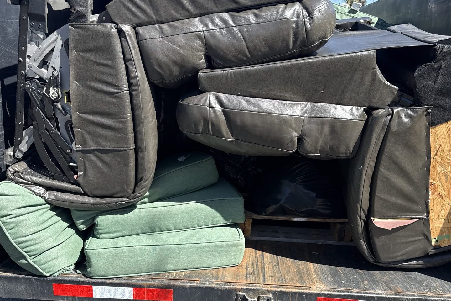 Leather sectional cushions and patio cushions loaded onto the bed of a DMD dump trailer