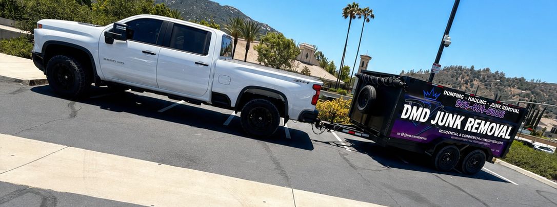 The DMD truck and dump trailer with the DMD JUNK REMOVAL wrap, pulling up to a job site in North County